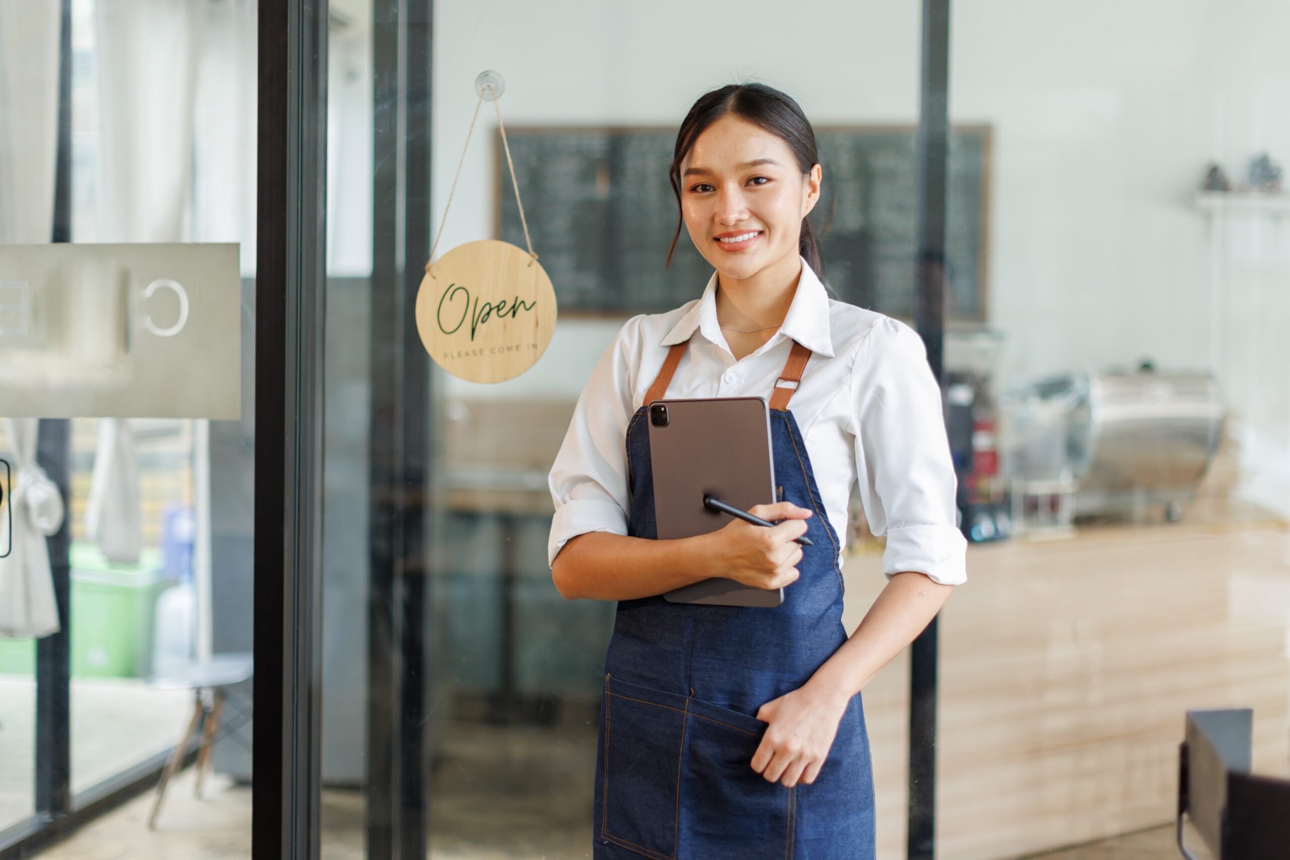 Image of Asian woman standing in front of her cafe with an open sign