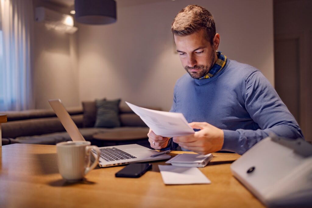 Man looking at paperwork in front of his laptop
